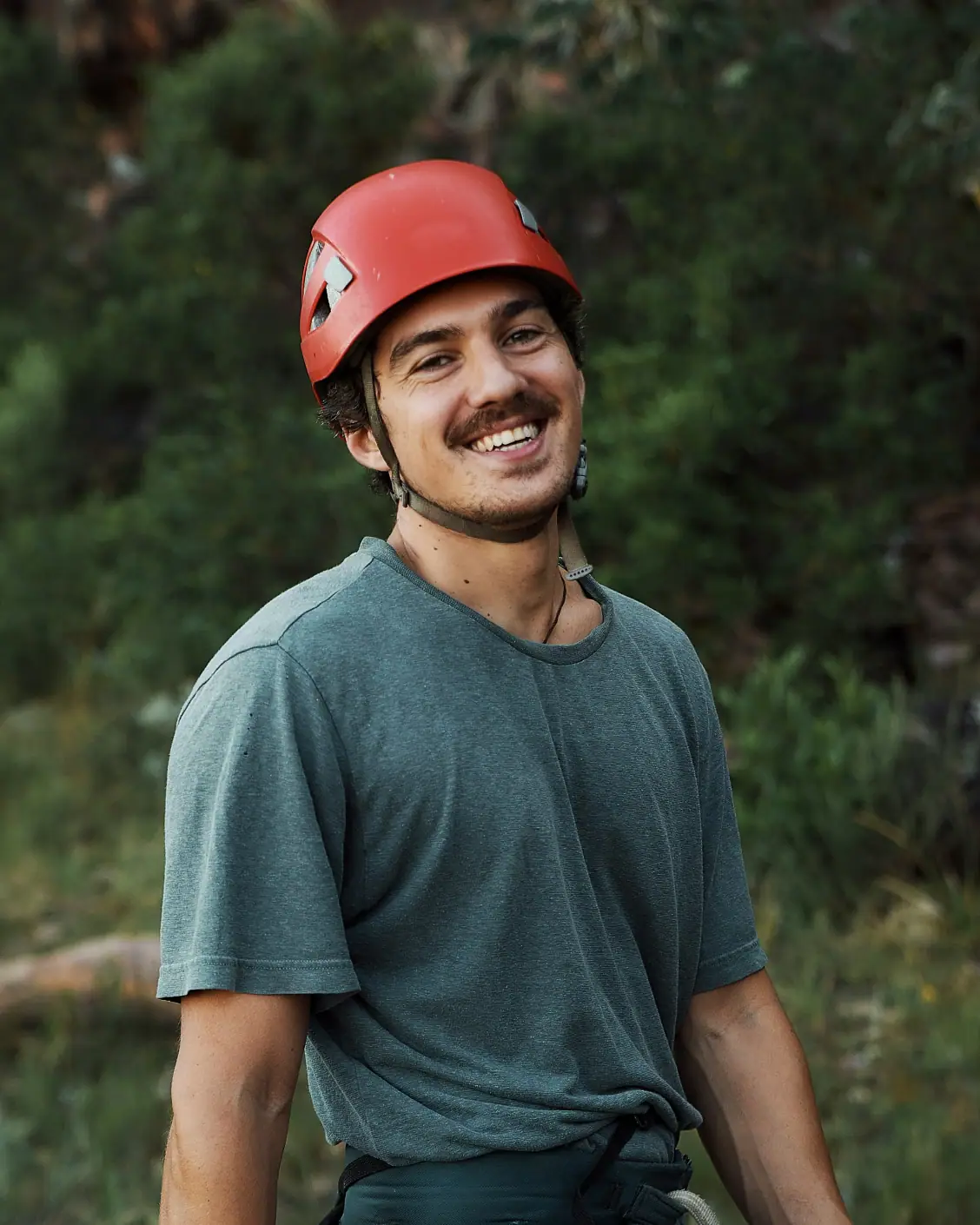 A smiling climber wearing a red helmet outdoors.